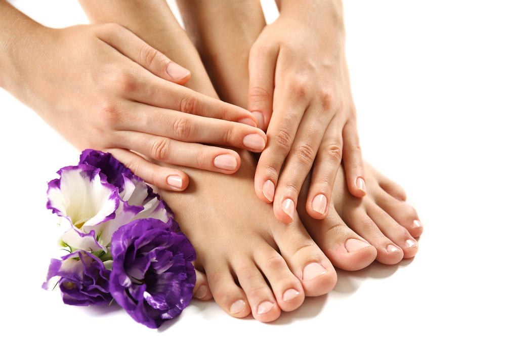 A close-up of a woman's feet adorned with purple flowers, featuring a single purple flower nearby, set against a neutral background.