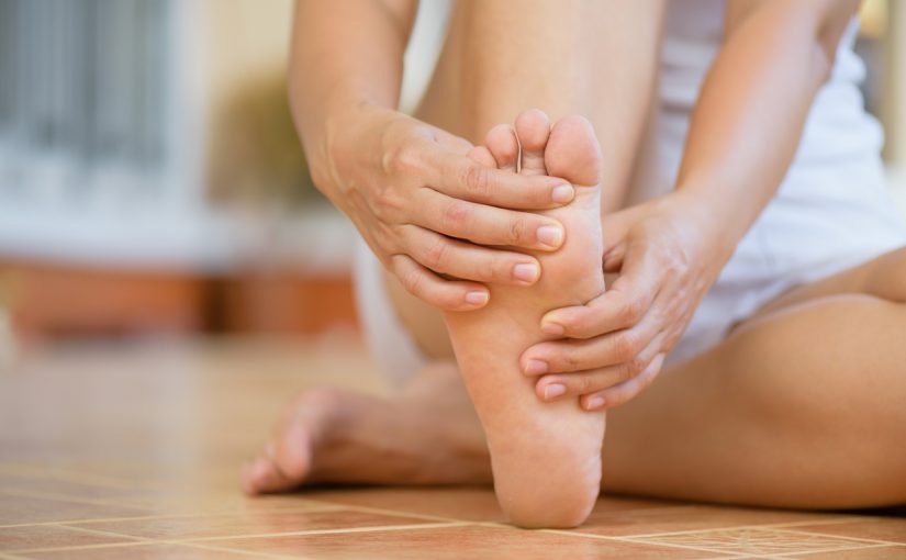 A woman sits down, holding her foot and gently rubbing it, indicating a moment of relaxation or relief.