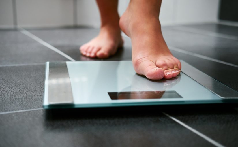 A person stands on a bathroom scale, measuring their weight in a well-lit bathroom setting.