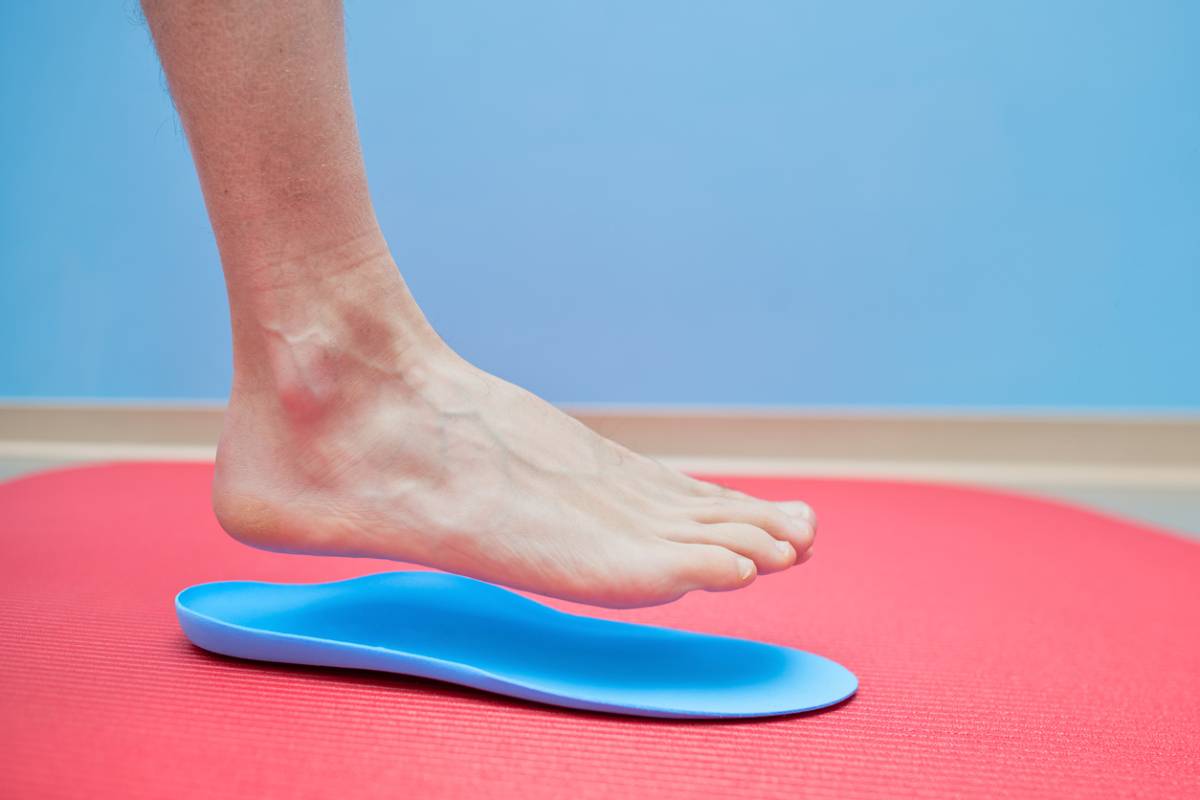 A person stands on a red mat, wearing a foot pad, demonstrating a balance or exercise technique.