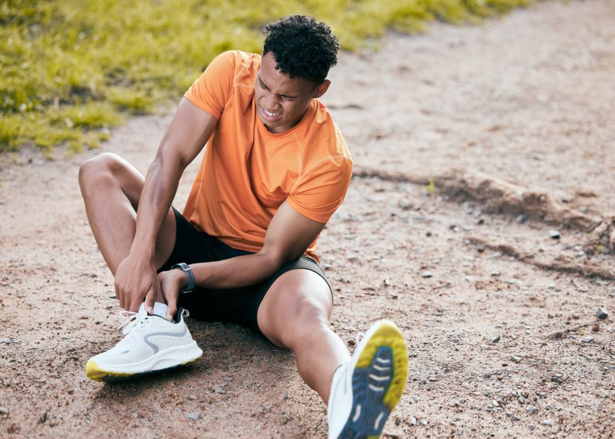 A man in an orange shirt kneels down, tying his shoe with focused attention.