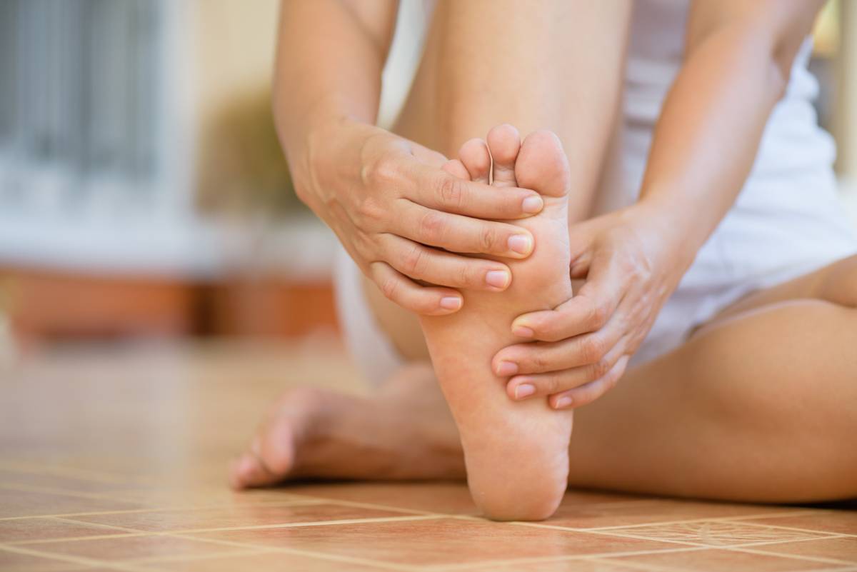 A woman sits down, holding her foot and gently rubbing it, indicating a moment of relaxation or relief.