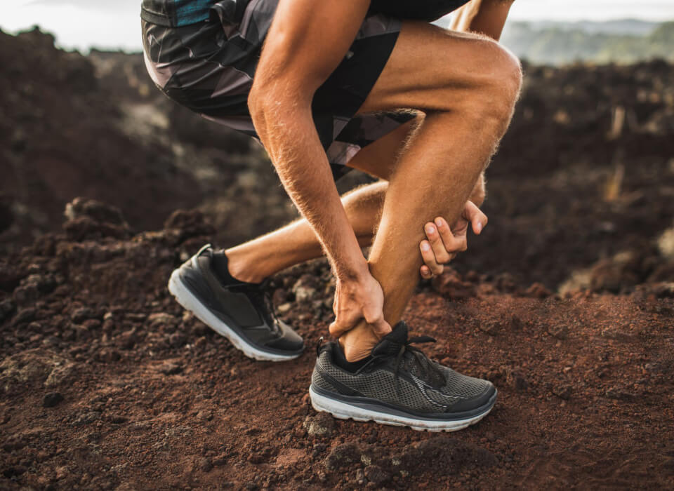 A man stretches his leg while running on a mountain trail, showcasing athleticism and the beauty of nature.