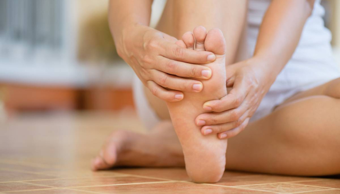 A woman sits down, holding her foot and gently rubbing it, indicating a moment of relaxation or relief.