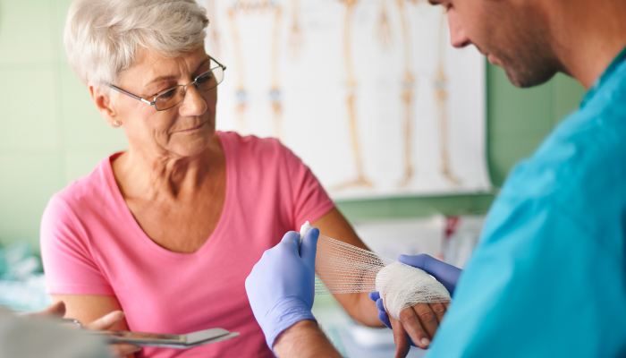 A doctor is carefully bandaging a woman's arm in a clinical setting, demonstrating attentive medical care.