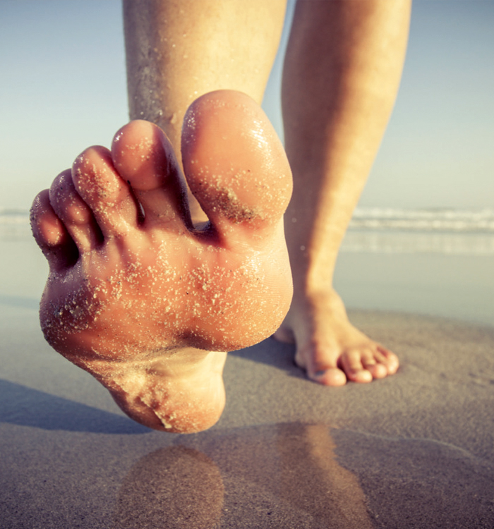 A person strolls along the beach, leaving footprints in the soft sand underfoot.