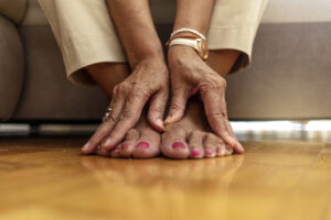 The image shows a close up of an older woman touching her feel to visually represent how foot health impacts overall health.